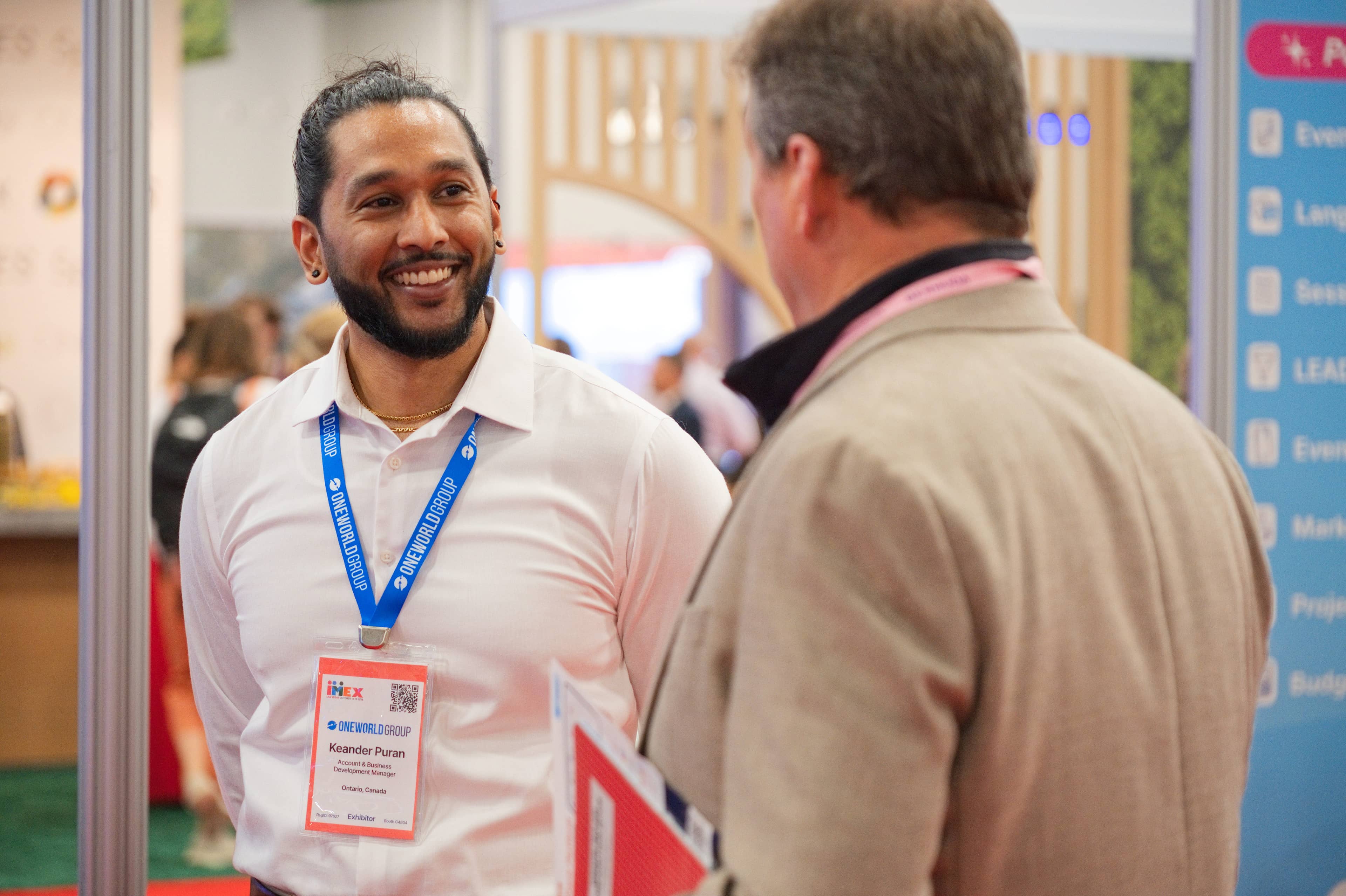 One World Group exhibitor smiling while speaking with a booth visitor